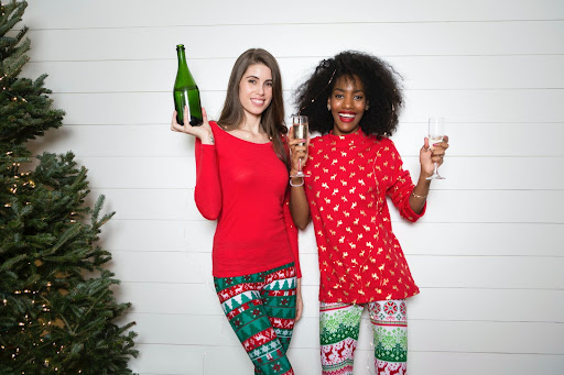 Two women holding a champagne bottle and flutes beside a Christmas tree